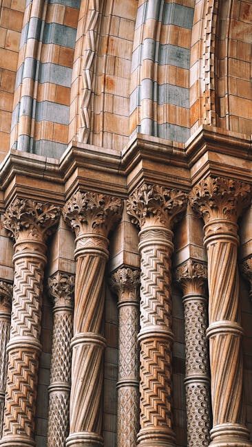Close-up image of an intricately carved stone column with a detailed capital, showcasing the ornate gothic architectural style. The column's surface displays a pattern of twisted and geometric designs, with alternating smooth and textured sections. The stone material appears aged but well-maintained, with a warm beige color and subtle weathering. Behind the column, part of a decorative stone wall with vertical striped motifs in shades of grey and beige is visible. The scene is well-lit, highlighting the craftsmanship and cleanliness of the surface, illustrating the importance of surface cleaning and maintenance in historic buildings. The image is relevant to domestic cleaning or surface sanitisation, as highlighted by Cleaners Knightsbridge in their explanation of cleaning quotes for authentic cost assessments.