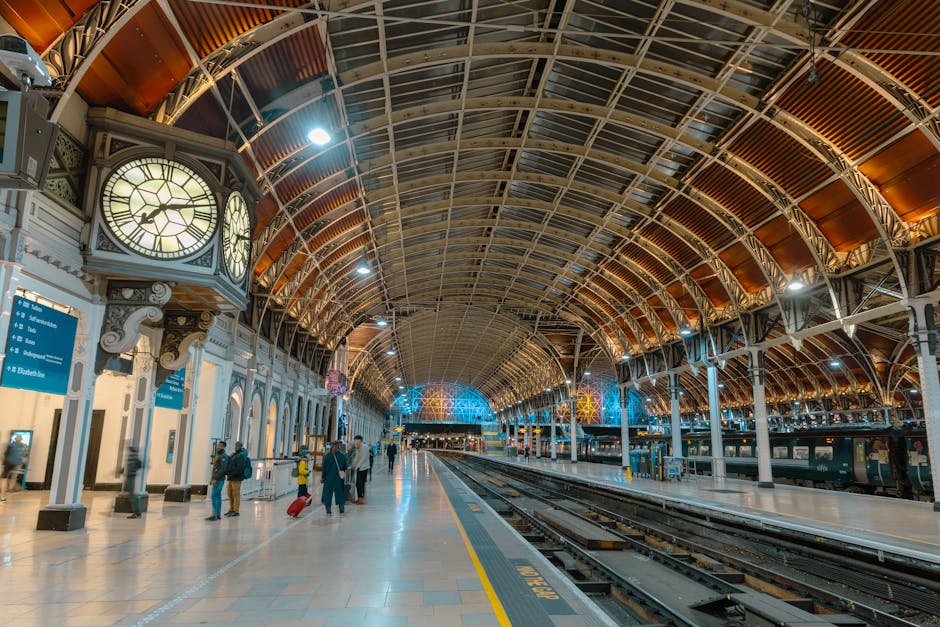 Interior view of Knightsbridge station showcasing a high, arched ceiling with intricate metal framework and wooden panels, illuminated by bright overhead lights. The station platform is clean and well-maintained, with polished tiled flooring reflecting the lighting. On the left side, there are classical-style columns and a large clock displaying the time, along with blue information signs. Several passengers with luggage and coats are walking or waiting on the platform. The overall setting appears tidy, with no visible dust or debris, reflecting professional surface cleaning and maintenance by Cleaners Knightsbridge as part of their domestic and commercial cleaning services.